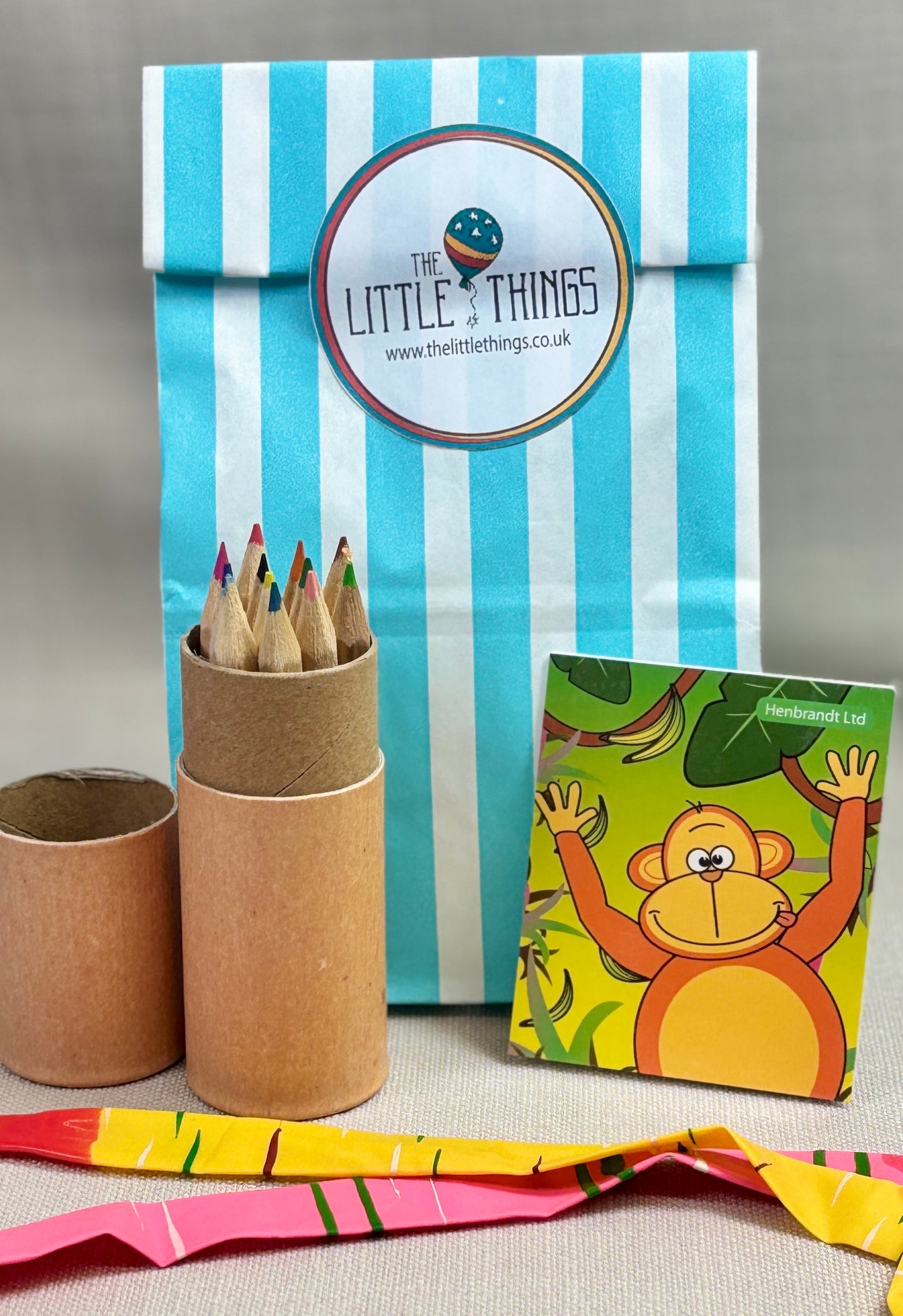 Party bag including a blue striped bag, cardboard tube with pencils, and a children's note book.