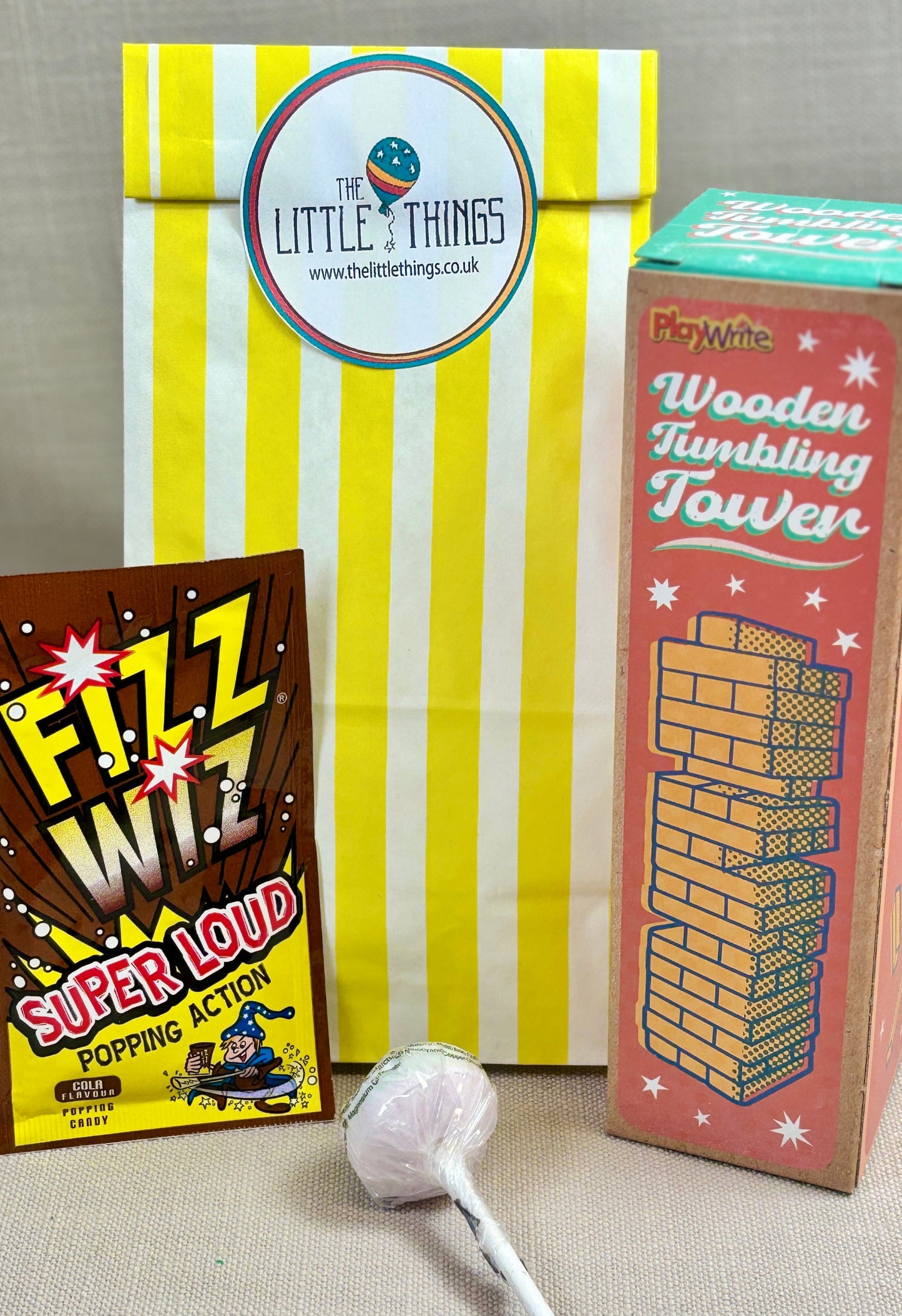 Three products includes a lollipop, 'Fizz Whizz', and a 'Wooden Tumbling Tower' with a Yellow striped paper party bag