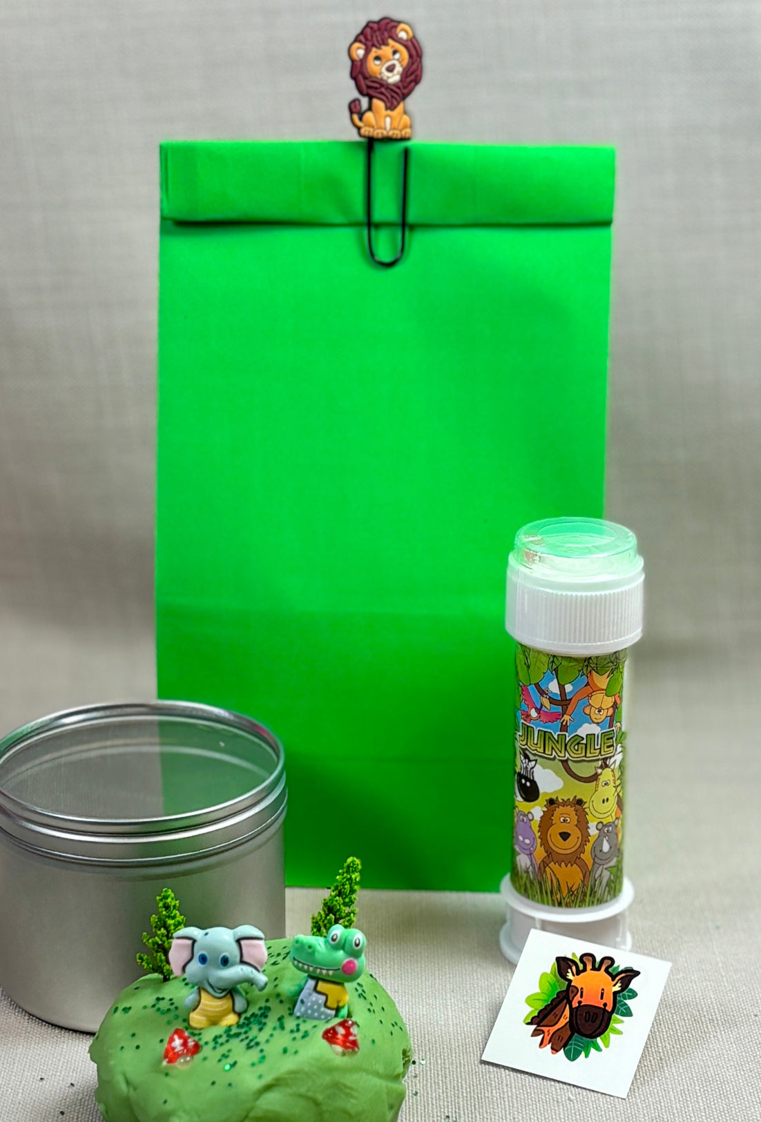 Green paper party bag with an animal paperclip. Bubbles, tattoo and a metal tin filled with Playdoh and mini toys for play.