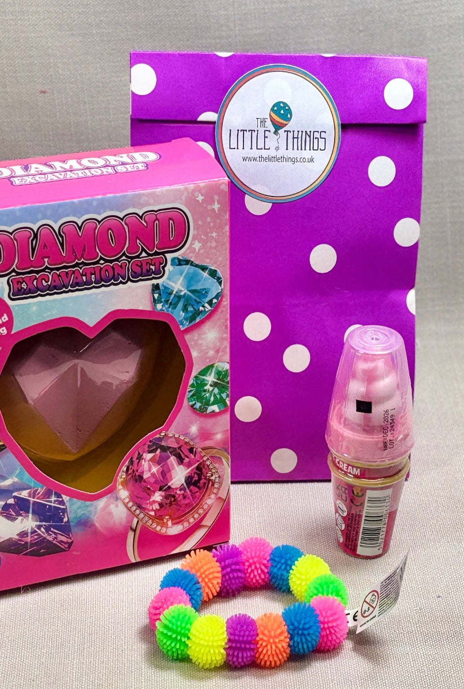 Girls Purple with white spots paper party bag will fillers. Including Colourful pom pom bracelet, Ice cream sweet pop, and a Excavation Gem dig.