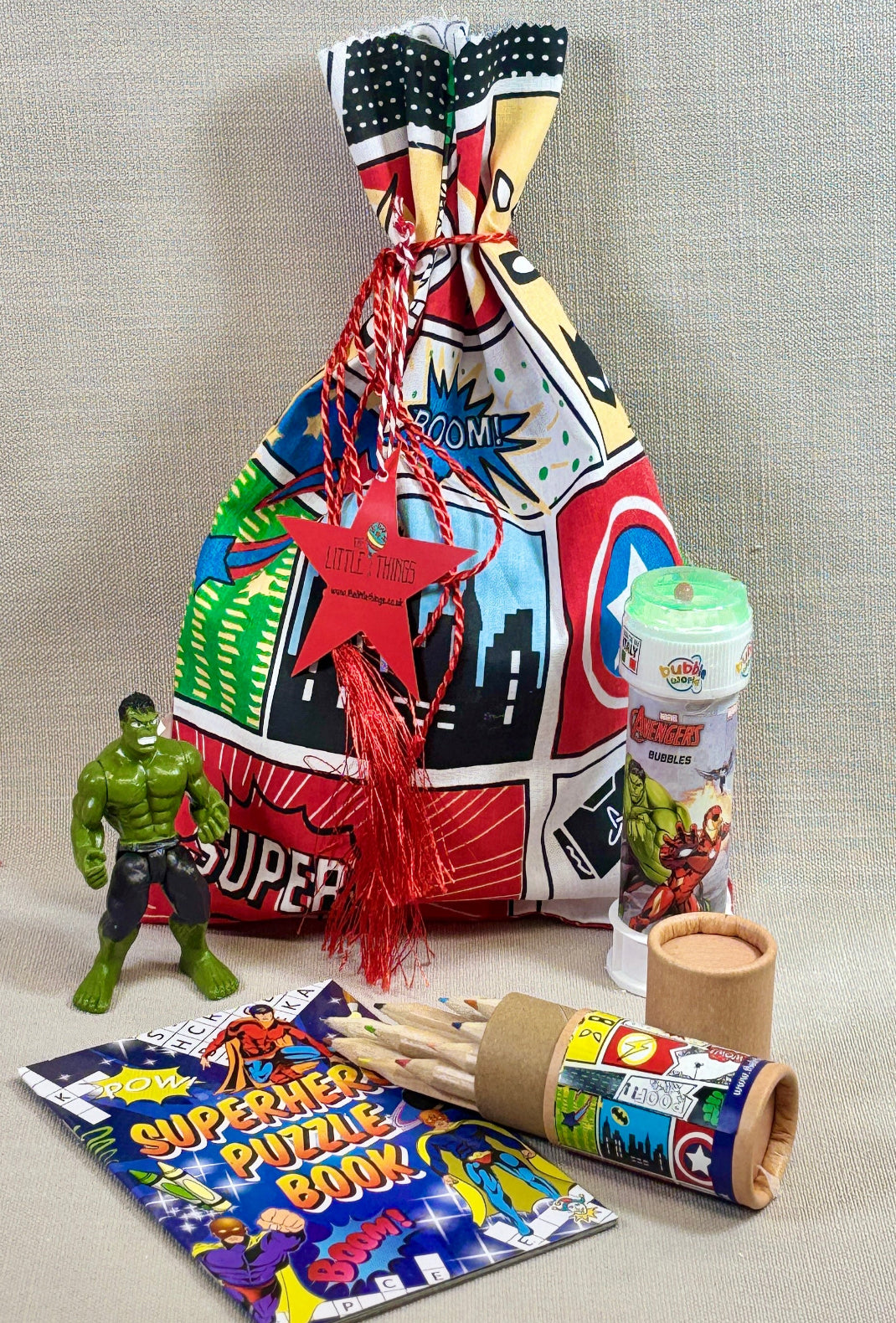 Colourful fabric gift bag with superhero design, toy figure, bubbles, colouring book and a tube of colouring pencils.