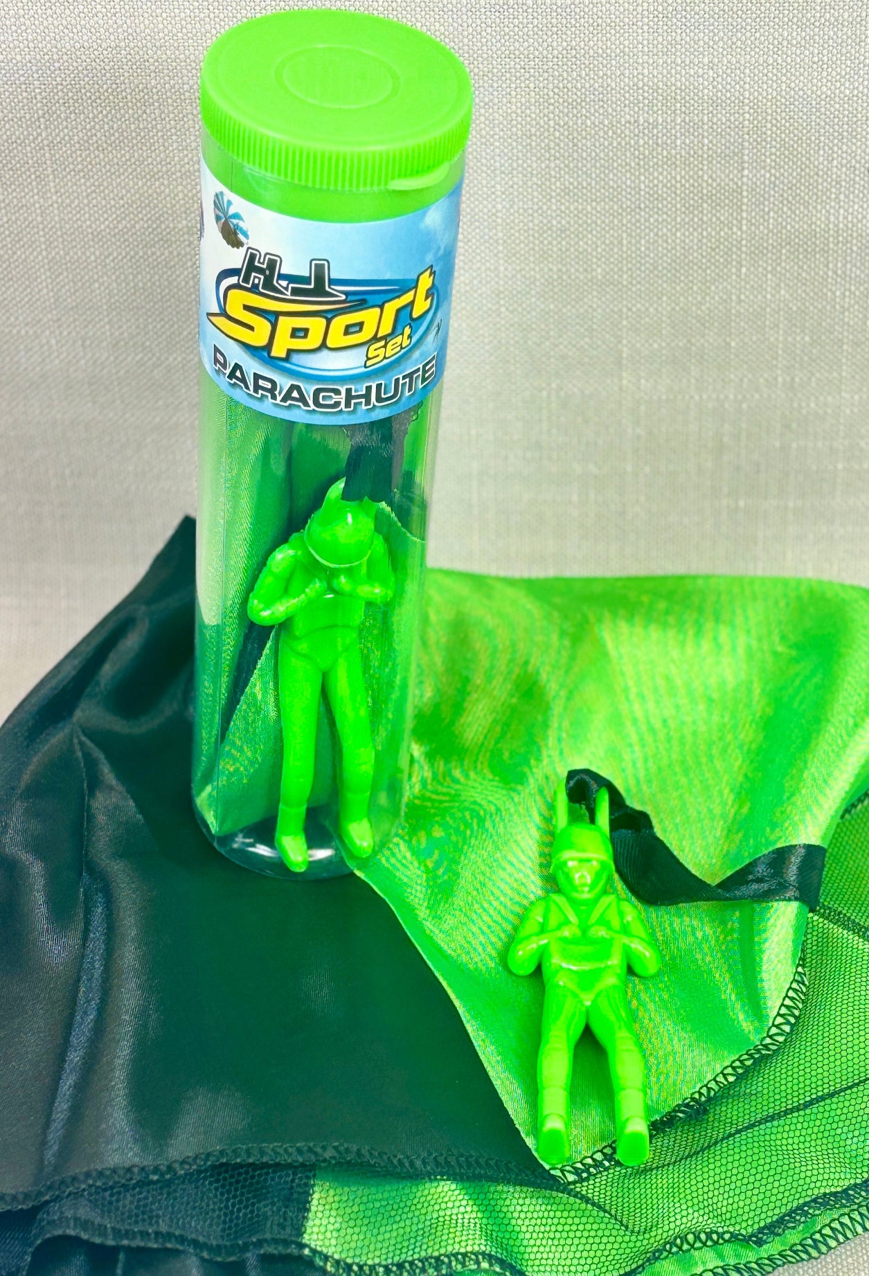 Green toy figures with a parachute and a container labeled 'Sport Parachute' on a light gray background.