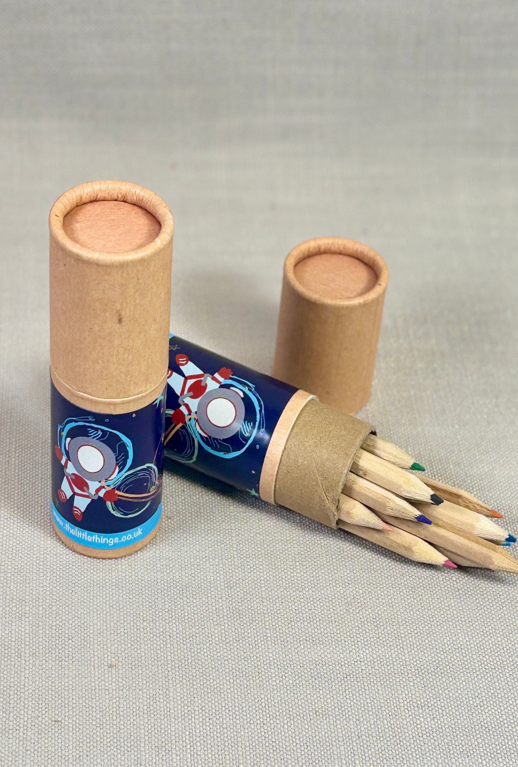 Two cardboard tubes with colorful designs, one open revealing wooden sticks on a gray background.