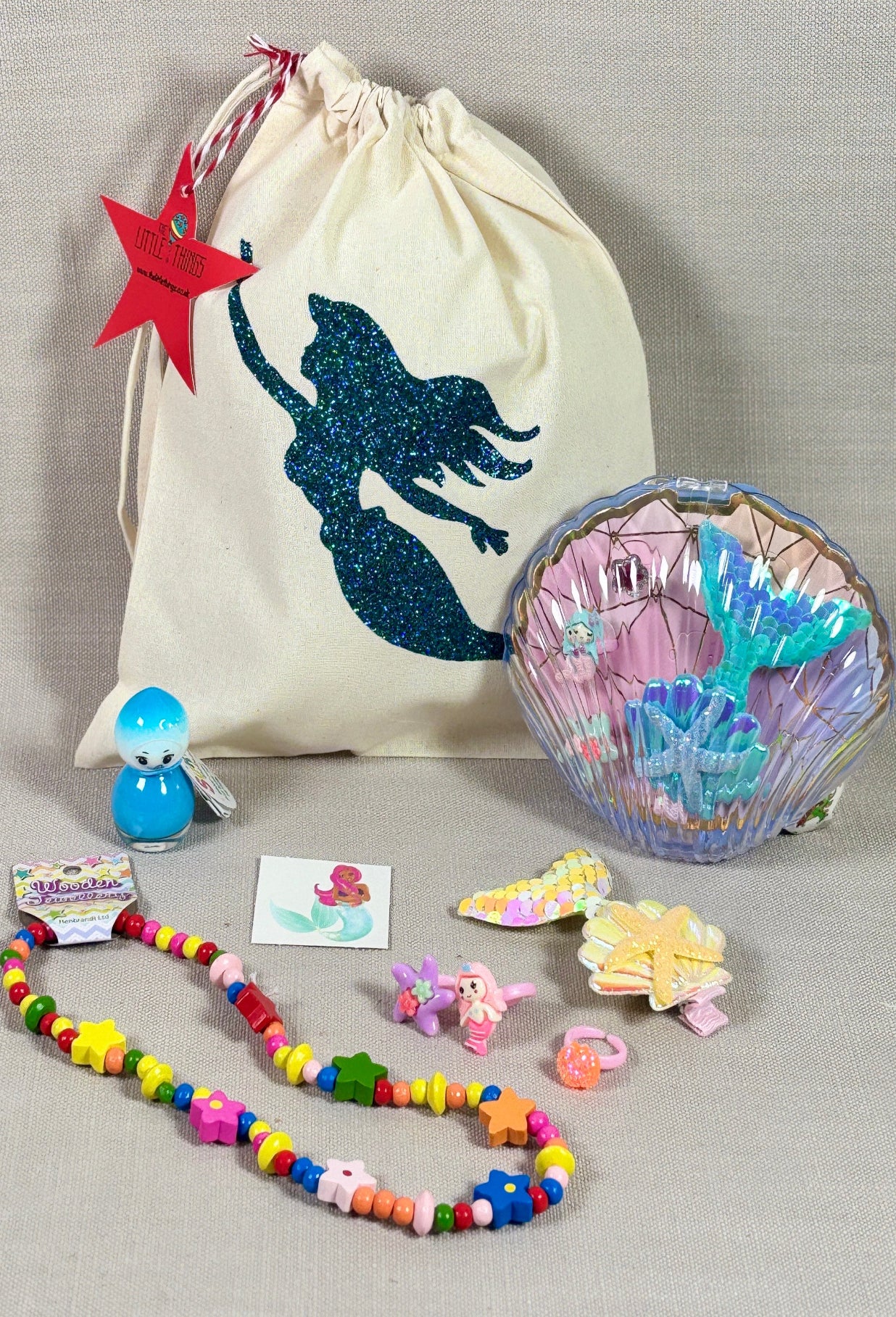 Mermaid-themed drawstring bag with accessories on a gray background