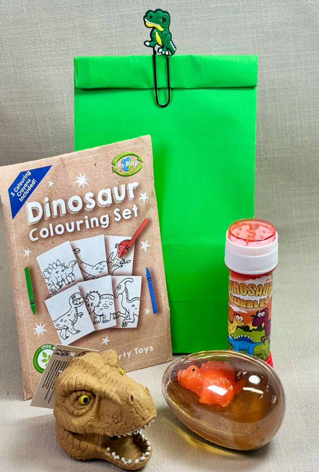 Green Paper party bag with dinosaur paper clip. Comes with Dinosaur colouring kit, bubbles, squeeze bead dino head and Dino egg slime with mini figure.