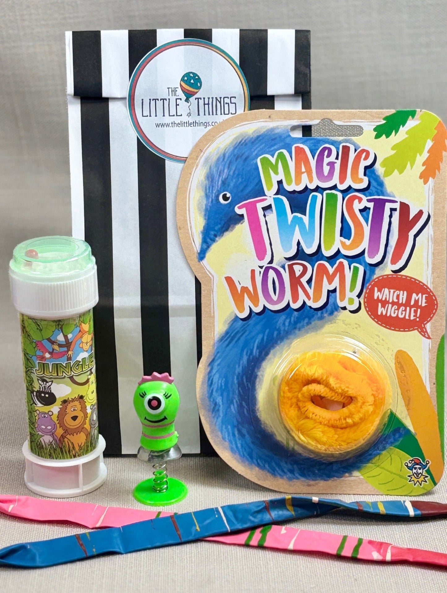 Children's black strip paper party bag, including a 'Magic Twisty Worm' package, a small green pop-up toy, and a tube of bubbles.
