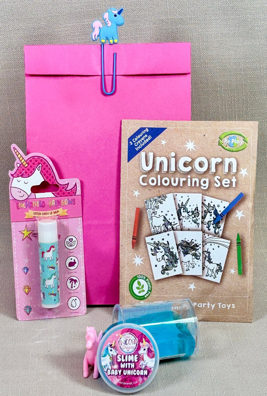 Pink paper unicorn paperclip party bag. With unicorn colouring kit, lip balm and a tube of unicorn slime.