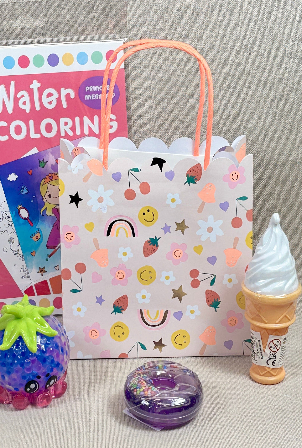 Coloring book, gift bag with ice cream design, and small toys on a gray surface