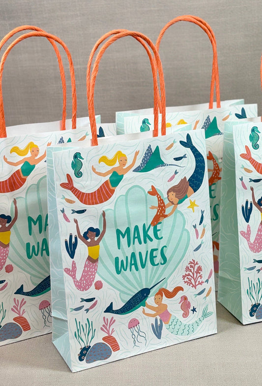 Three paper gift bags with mermaid illustrations and 'Make Waves' text on a neutral background.
