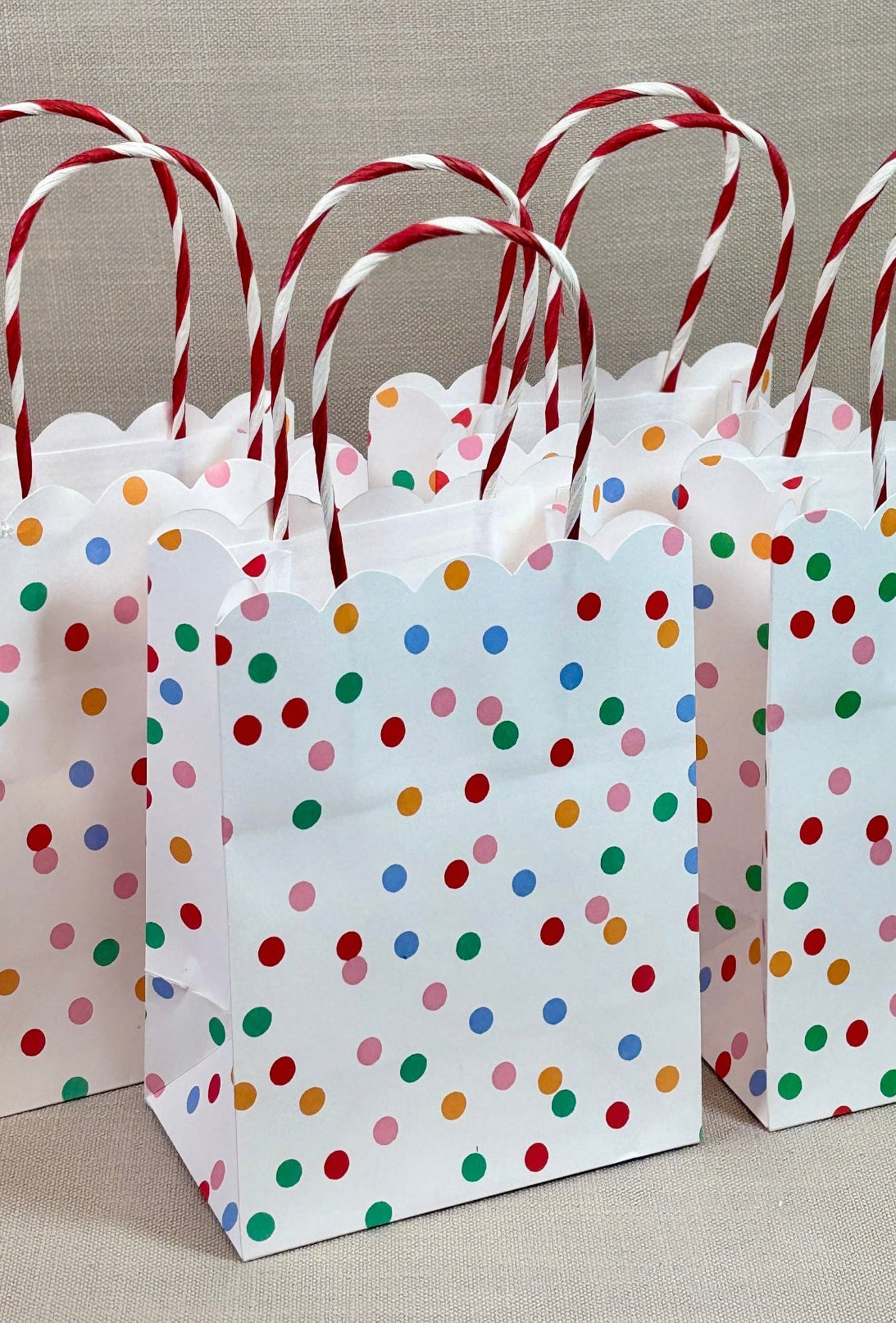Three white paper bags with colorful polka dots and red handles.