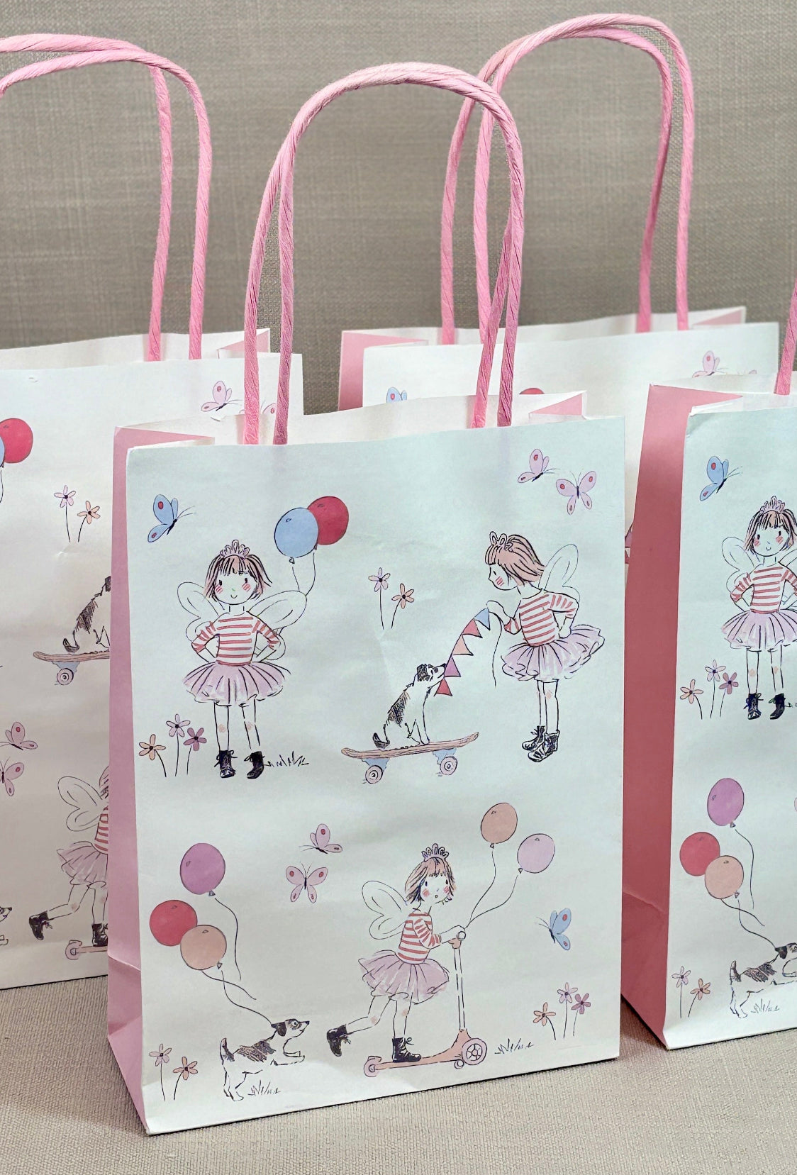 Set of three paper bags with pink handles and illustrations of a girl with balloons.