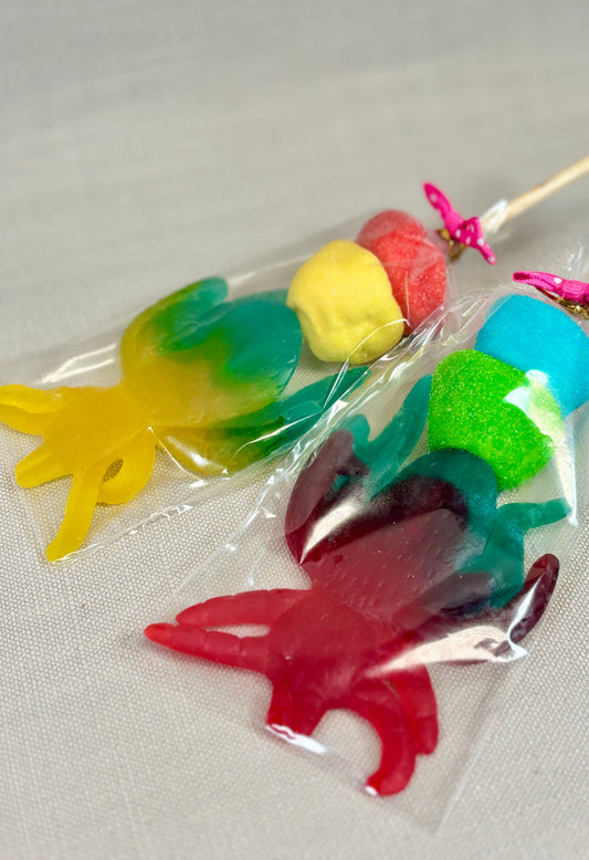 Colourful jelly sweet spider-shaped lollipops, with two colourful marshmallows in a clear bag, tied with a bow.