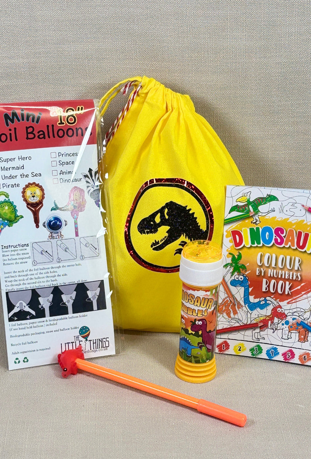 Children's party favor set with balloons, a yellow drawstring bag, and coloring book on a gray background