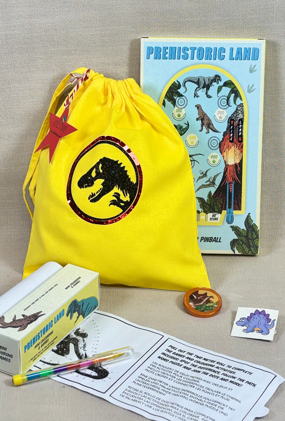 Dinosaur-themed educational kit with yellow drawstring bag, book, and toys on a gray surface.