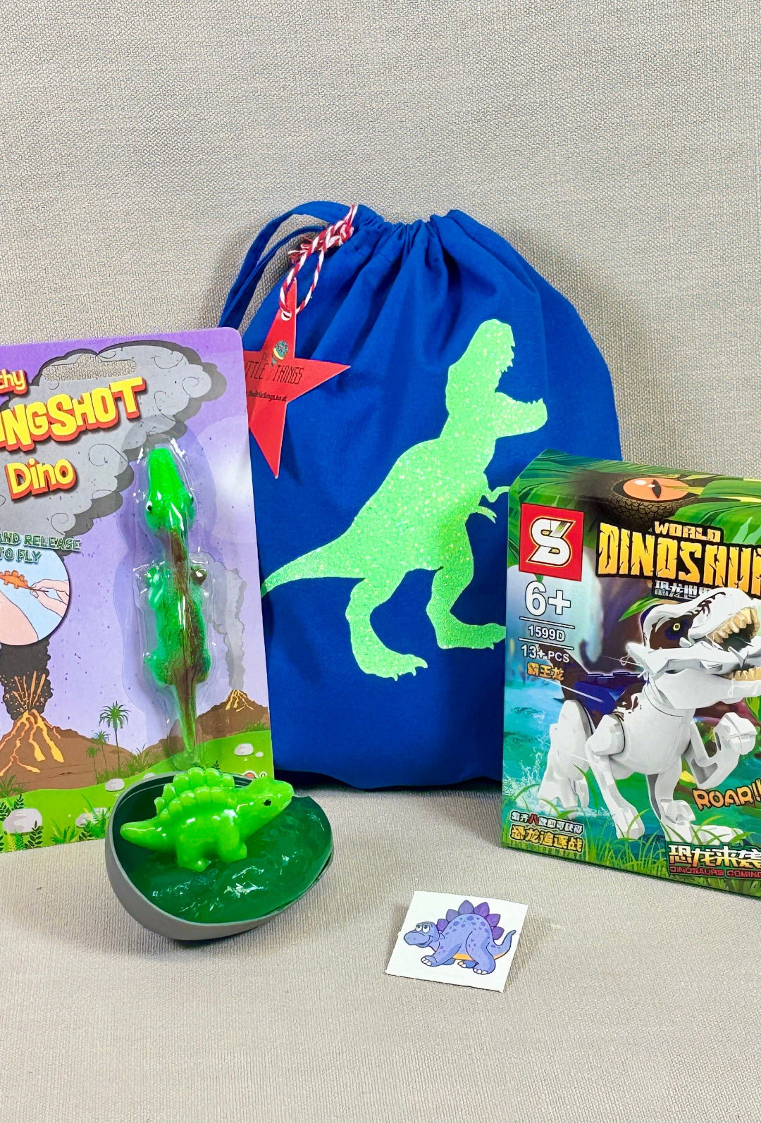 Dinosaur-themed toys and accessories including a toy, packaging, and drawstring bag on a gray background.
