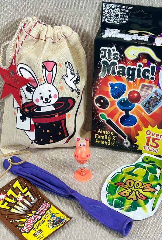 Assorted magic-themed toys and items including a drawstring bag, box, and colorful packets on a gray surface.