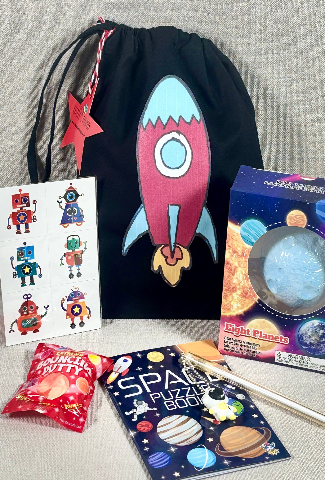 Space-themed children's activity kit with a drawstring bag, book, stickers, and paint set on a gray background.