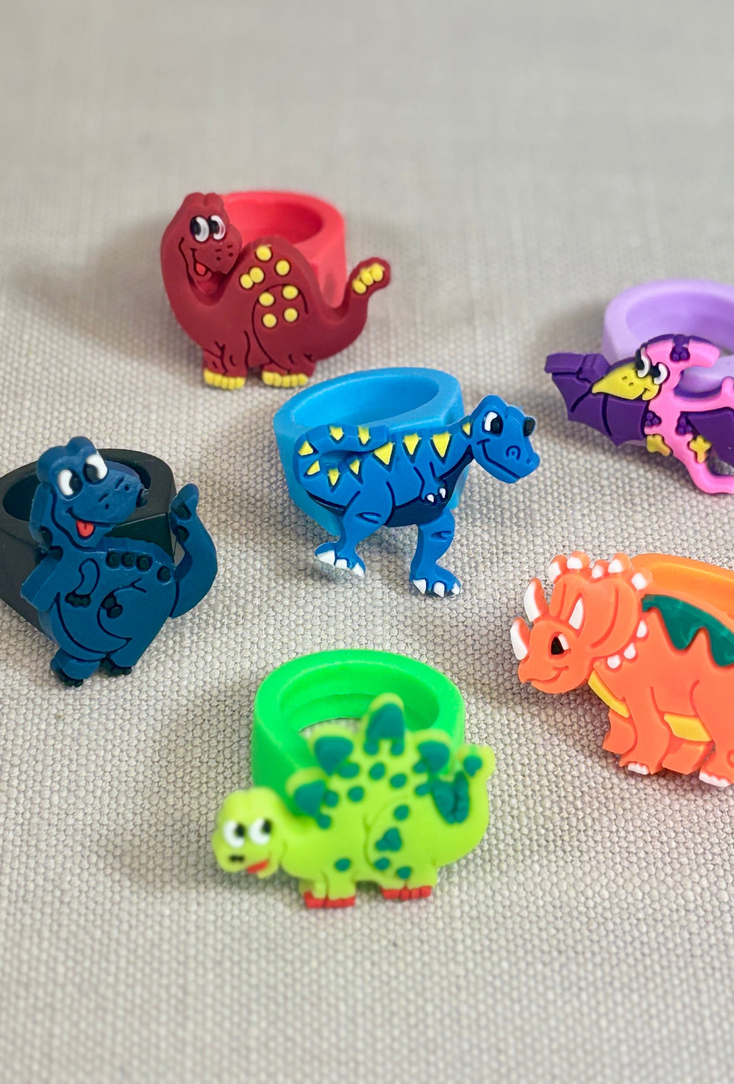 Set of colorful dinosaur-shaped rings on a beige fabric background