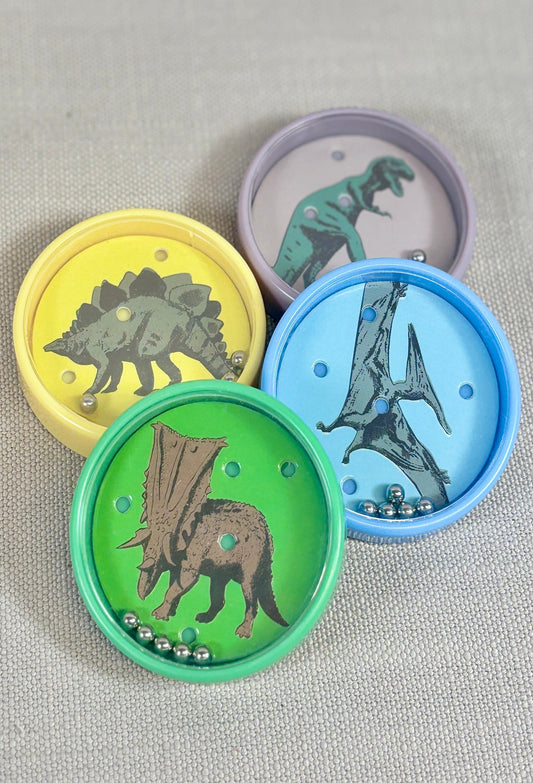 Four colorful tilt puzzles with dinosaur designs on a gray fabric background