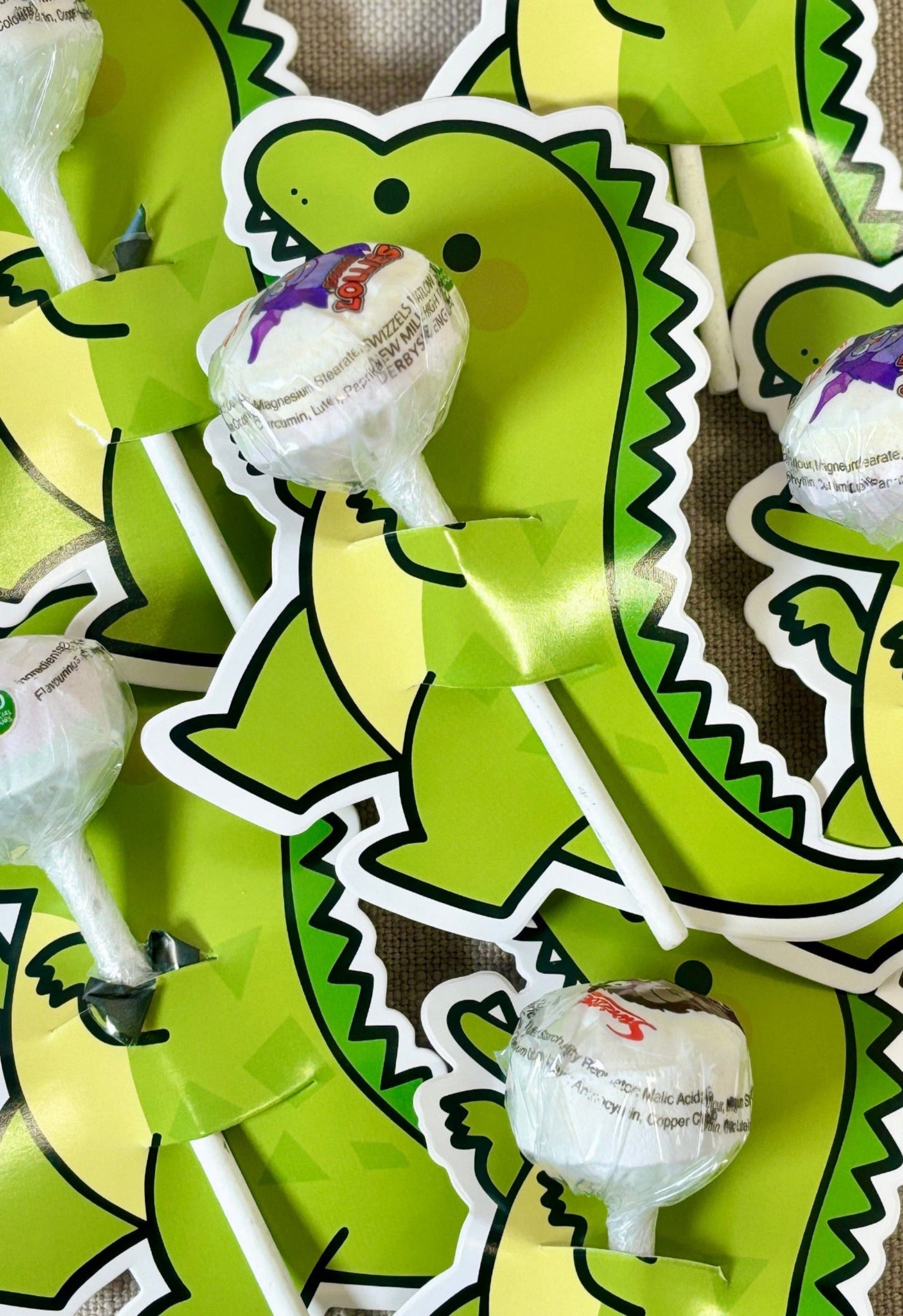 Dinosaur-shaped lollipop sticks with white suckers on a beige background