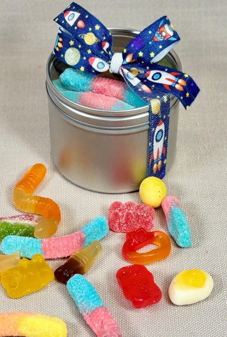 Metal tin with colorful candies and a polka dot ribbon on a gray background