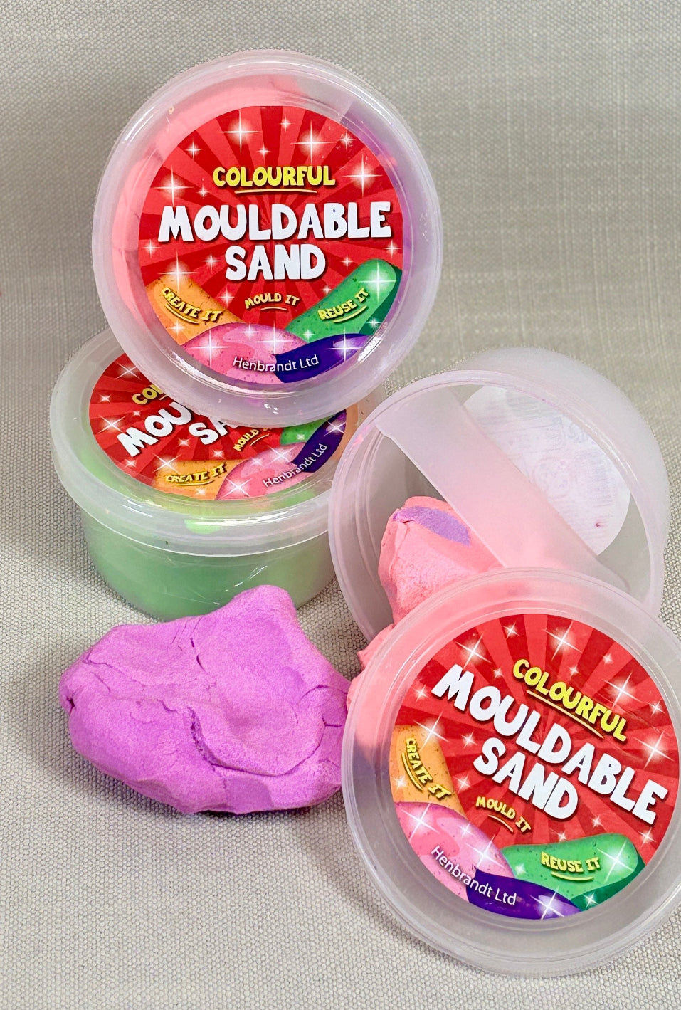 Three containers of mouldable sand with colorful labels on a gray background