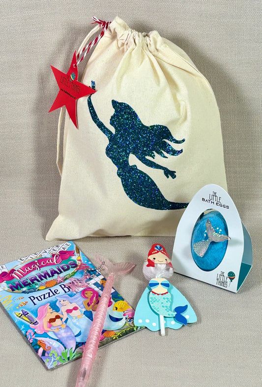 Mermaid-themed items including a drawstring bag, puzzle, pen, and figurine on a beige surface.