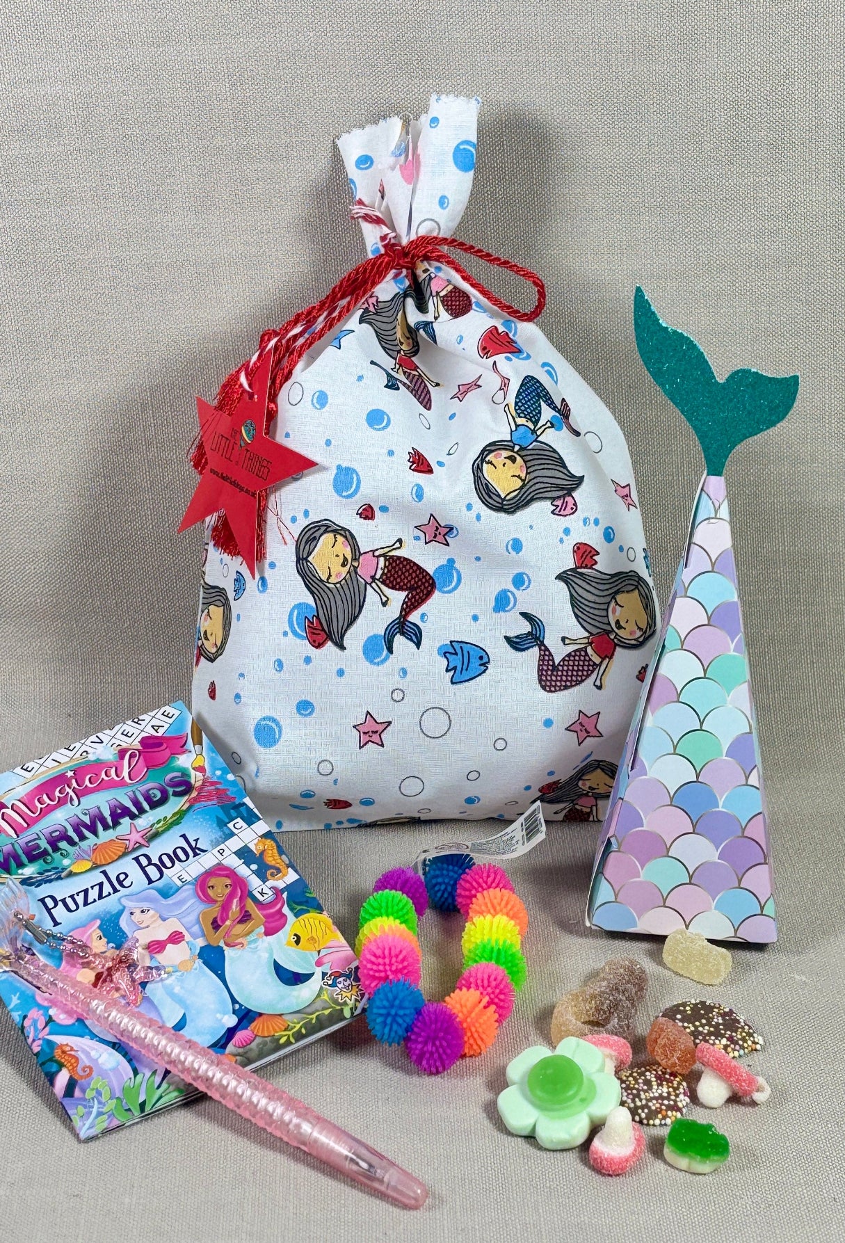 Mermaid-themed gift bag with accessories on a gray background