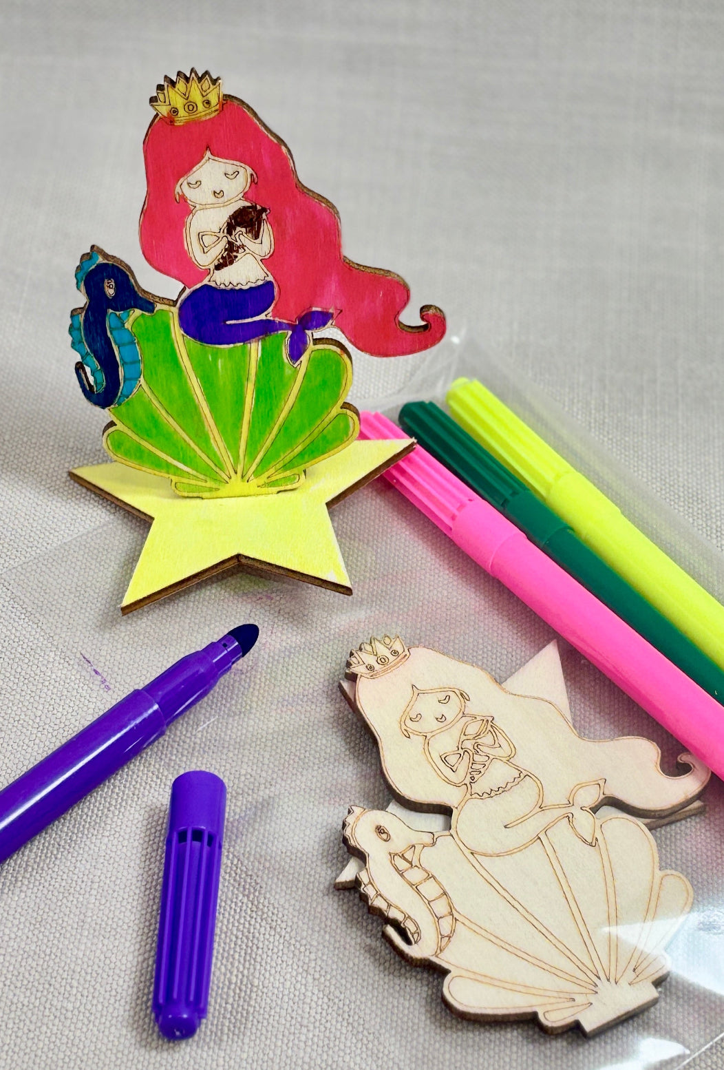 Colorful pens and wooden mermaid figures on a gray background