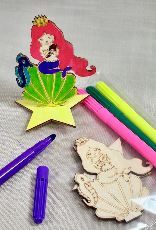 Colorful pens and wooden mermaid figures on a gray background