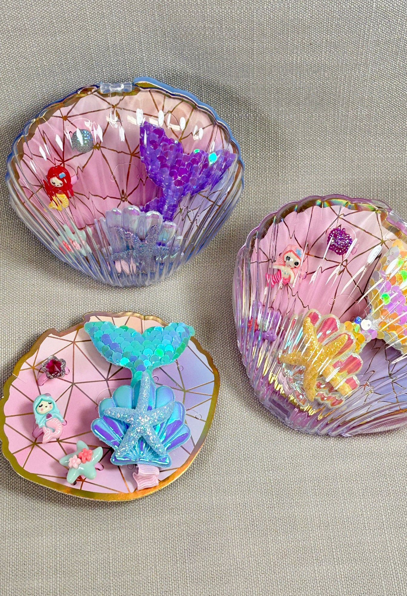 Three colorful shell-shaped jewellrey dishes with decorative items on a gray background