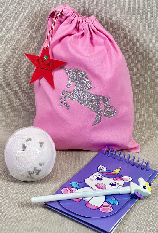 Pink drawstring bag with unicorn design, Large bath bomb, and purple notebook with unicorn pen.
