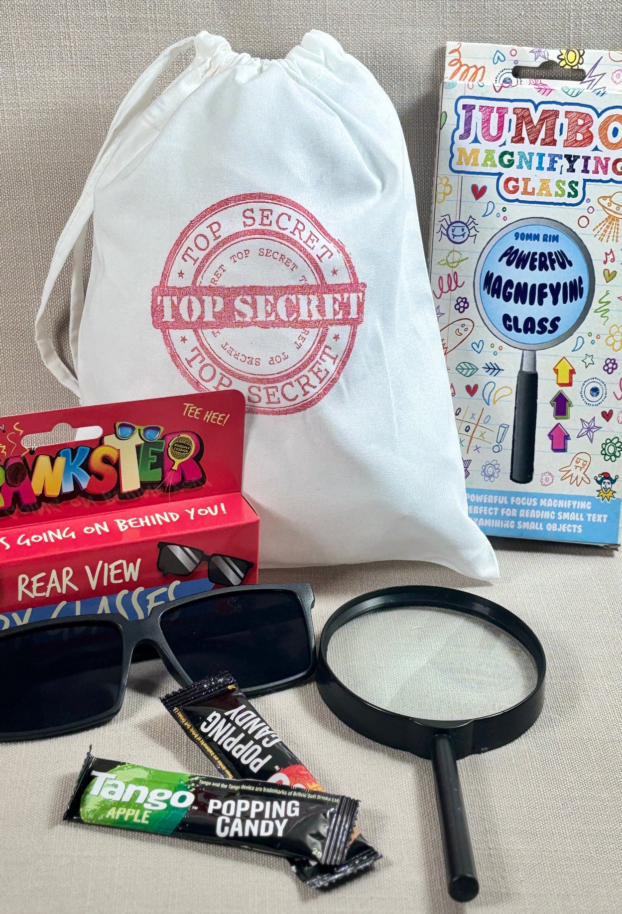 Top Secret bag with candy, magnifying glass, and Jumbo Magnifying Glass packaging on a textured surface.
