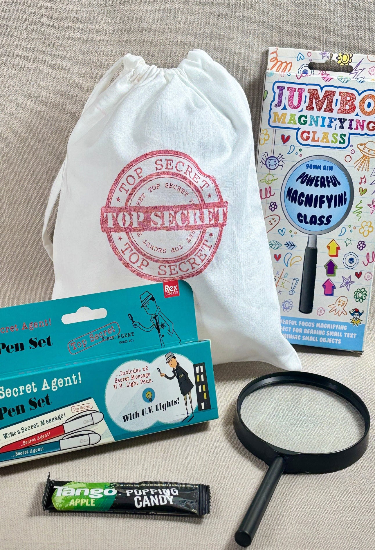 Top Secret stamped white fabric party bag with spy pen set, candy, and magnifying glass.