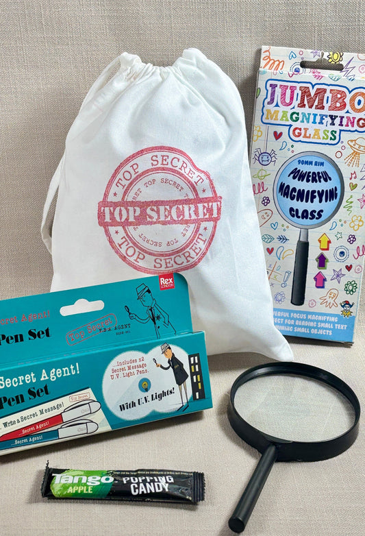 Top Secret stamped white fabric party bag with spy pen set, candy, and magnifying glass.